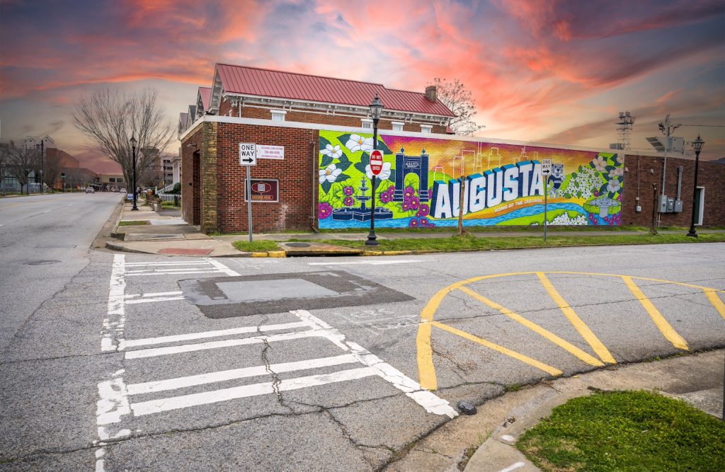A mural on the side of a building with flowers, a brick archway, a mascot depicting a jaguar and the words "Augusta."