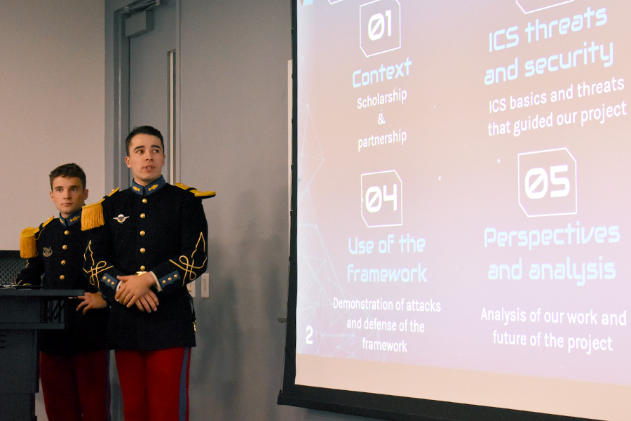 Two men in French military uniforms stand at the front of a classroom, presenting in front of a screen.