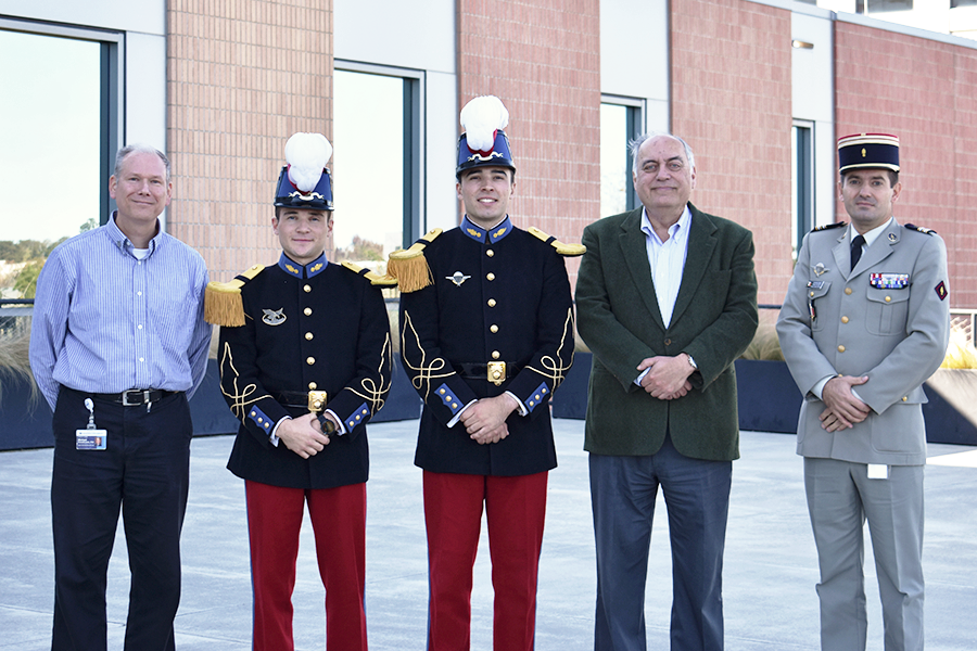 Five men, three in French military uniforms, pose for a photo outside.