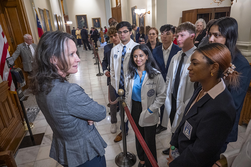 A woman speaks with college students outside a large government auditorium.