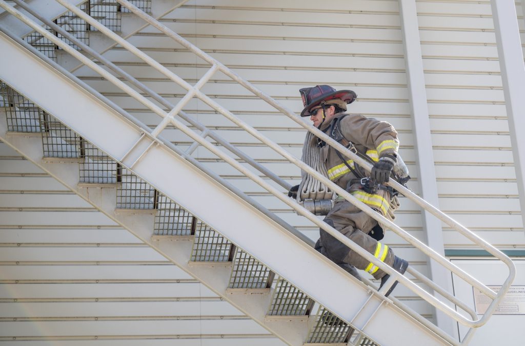 Firefighter in full gear runs up tower with a hose.