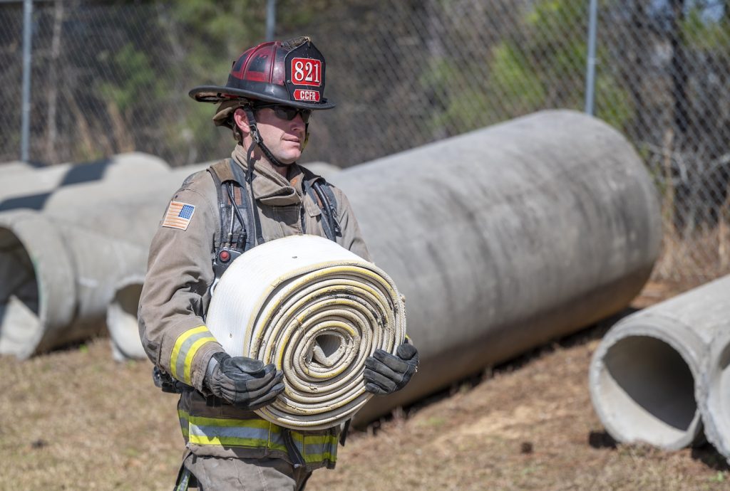 Firefighter in full gear carries a rolled-up fire hose.