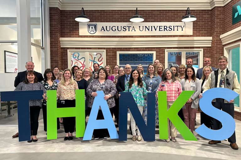 A large group of people stand behind large letter that spell out "Thanks."