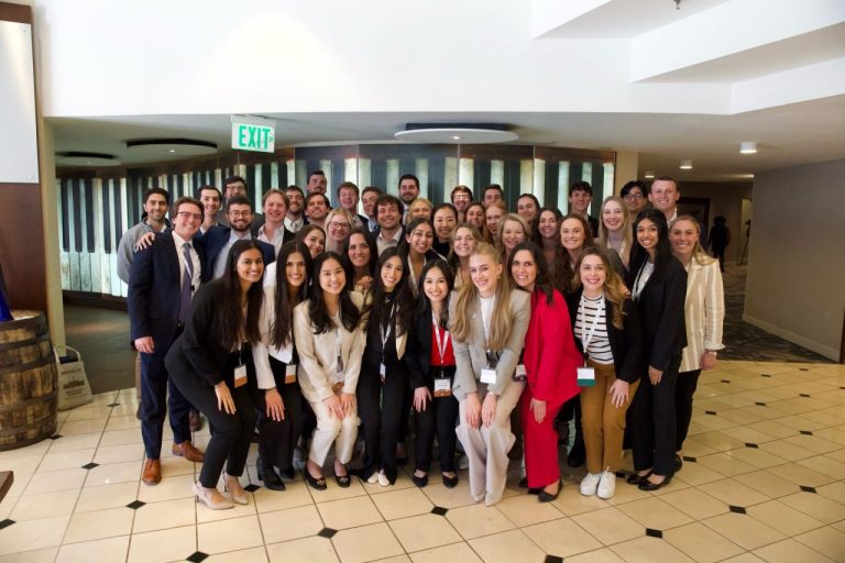 A few dozen people in business attire stand together for a group photo.