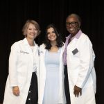 Three women in white coats pose for a photo