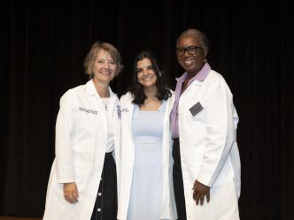 Three women in white coats pose for a photo
