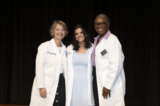 Three women in white coats pose for a photo