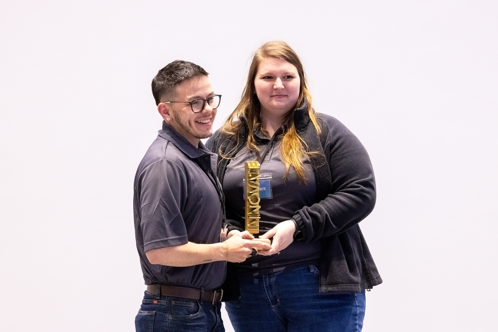 A male and female college student pose with a trophy during an awards ceremony after a competition.