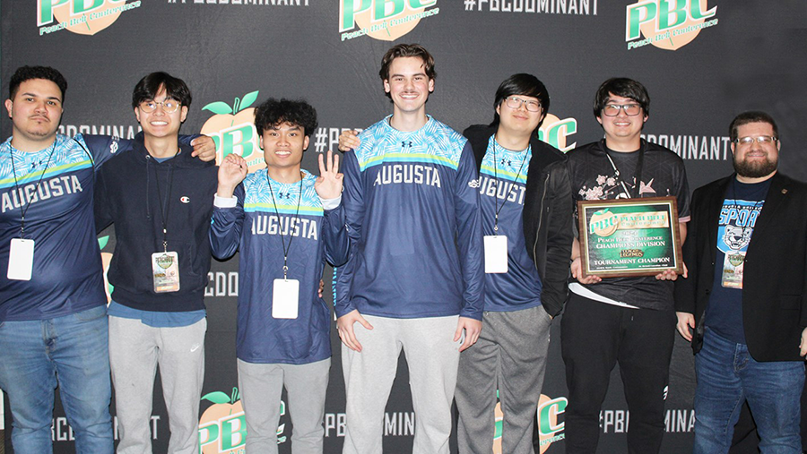 Six college students wearing long-sleeved esports jerseys stand with their coach celebrating having won a championship.