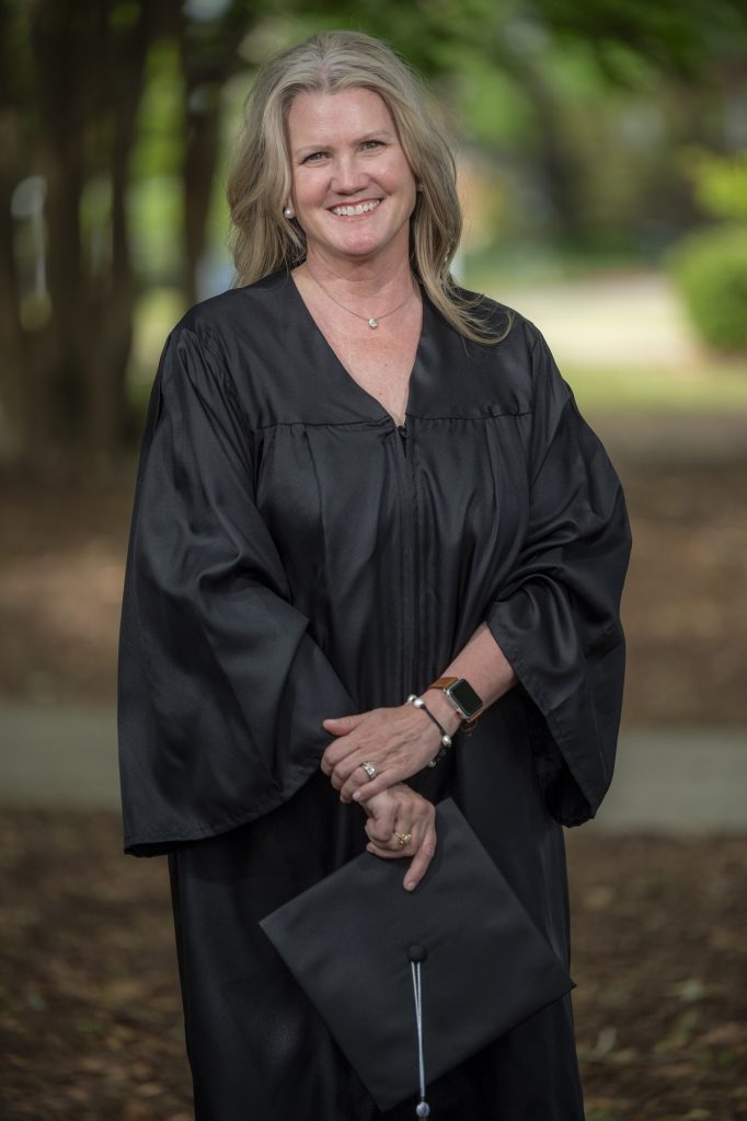 A woman wearing a graduate robe poses for a photo outside.
