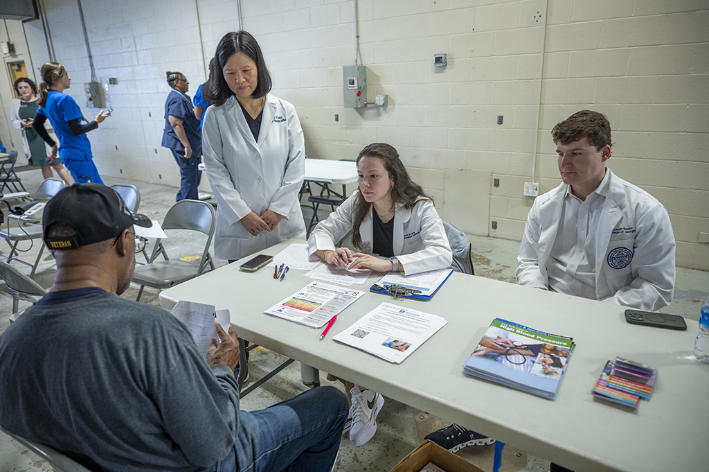 Two women and a man in white lab coats talk to a man looking over paperwork