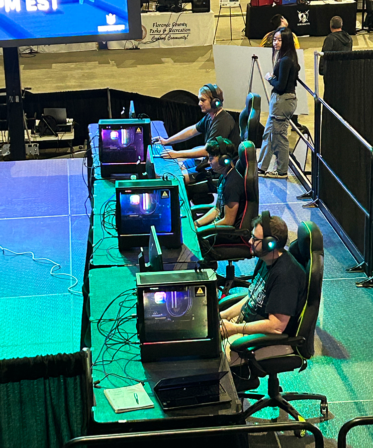 Three college students sit at gaming computers inside an arena waiting for an esports competition to begin.