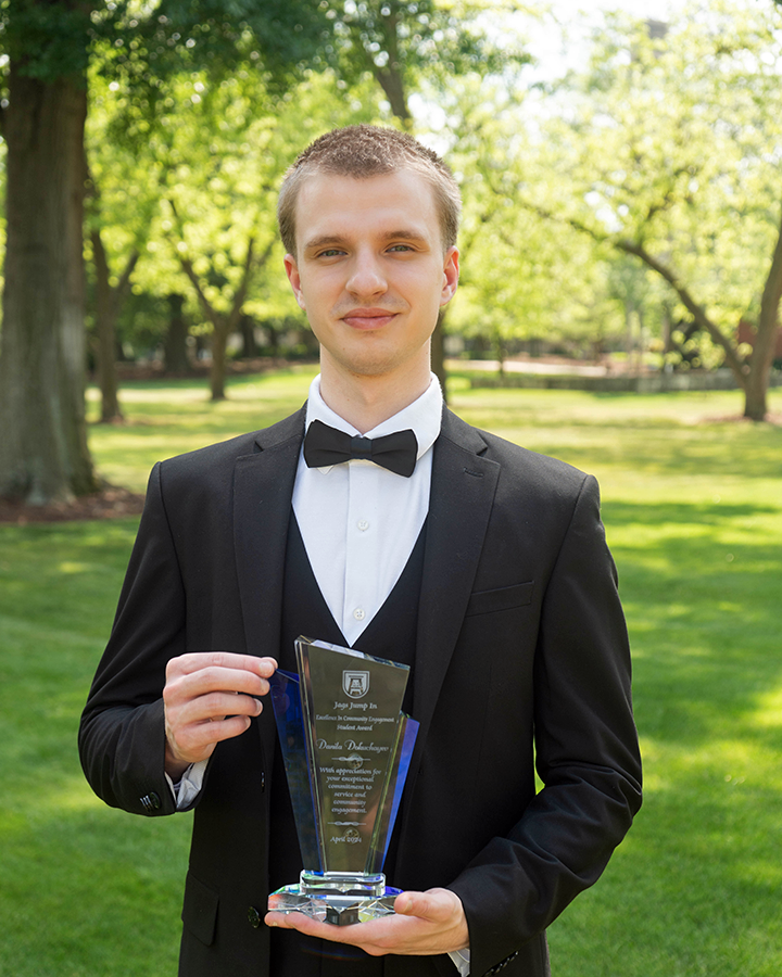 a man standing outside in a tuxedo with a bow tie holds an award