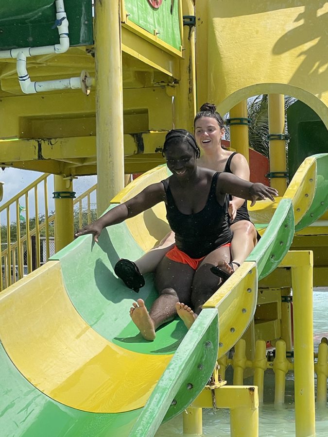 a female student helps a female resident slide down a green and yellow waterslide