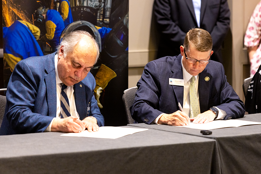 Two men sign papers during a ceremony.