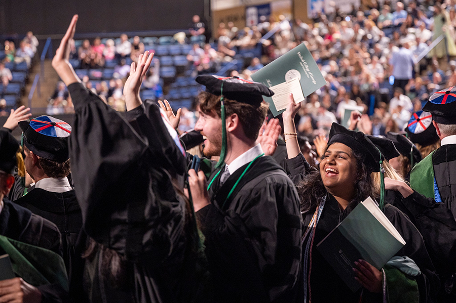 A recent medical school graduate celebrates by waving to her family in a large crowd.