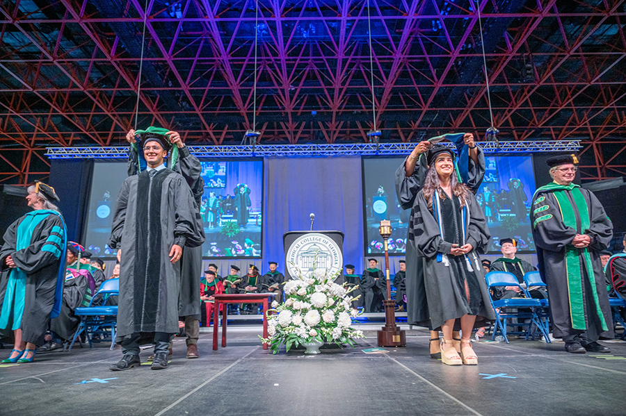 Recent medical school graduates have ceremonial hoods placed over their shoulders.