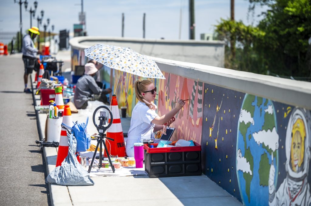 People paint murals on a wall of a pedestrian bridge.
