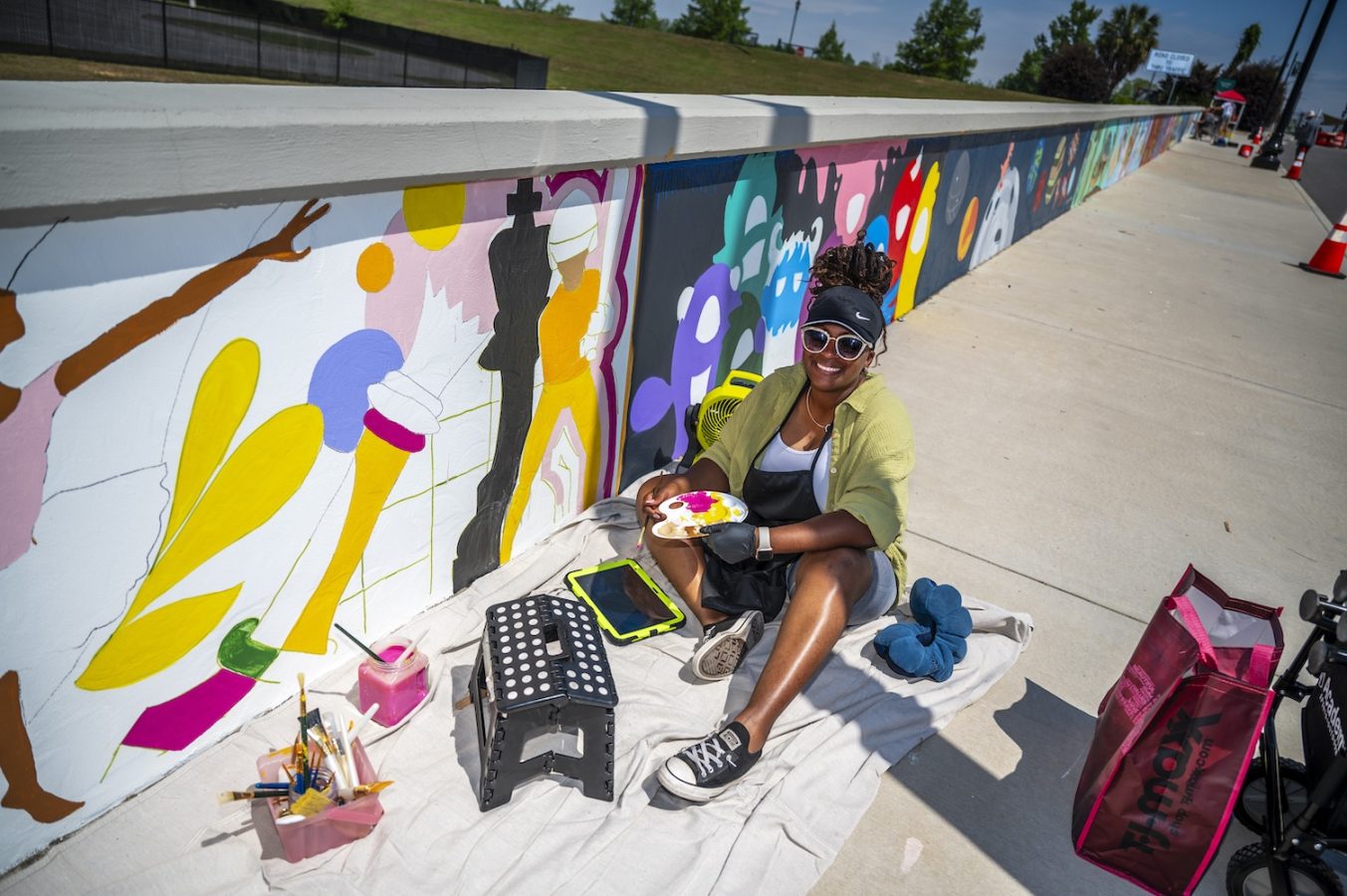 A woman paints a mural along a wall of a pedestrian bridge.