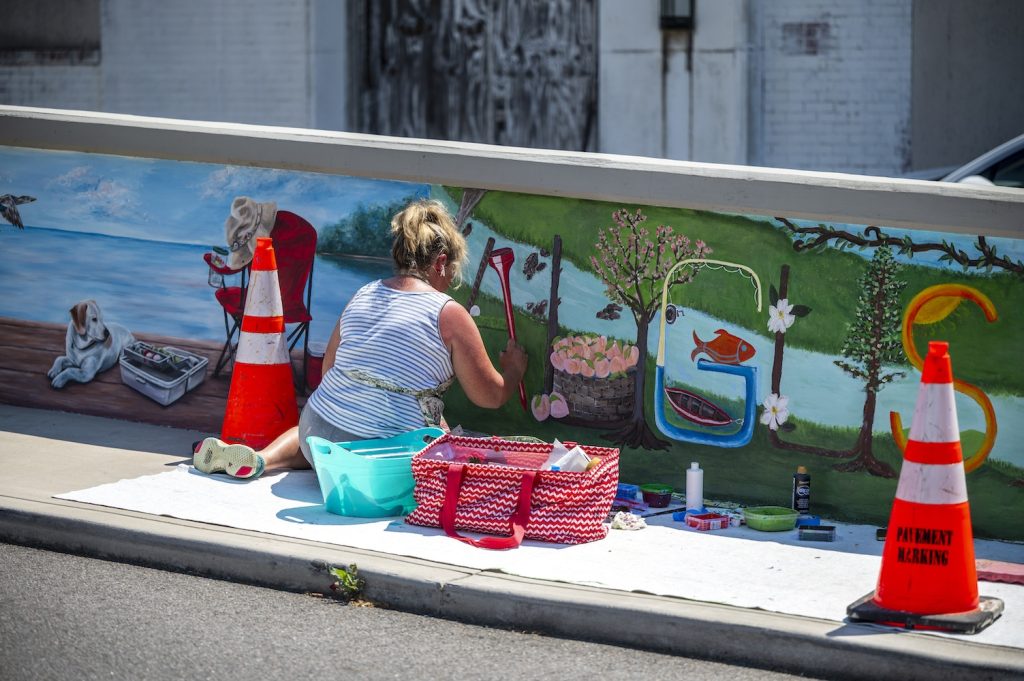 A woman paints a mural on a wall of a pedestrian bridge.