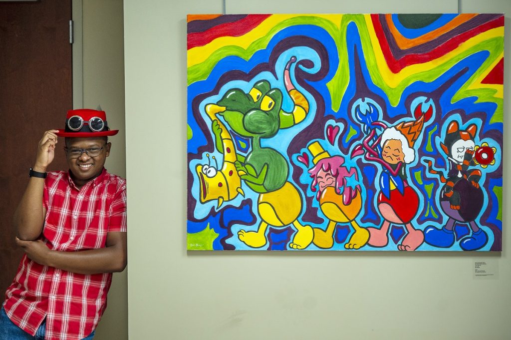 A young man leans against a wall next to a painting of cartoon animals playing musical instruments.