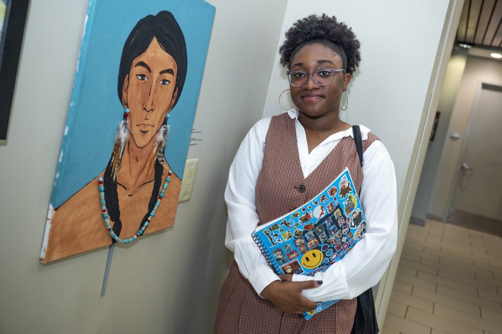 A young woman stands next to a painting she created.