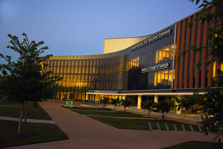 Sunset over a large, modern education building on a medical college campus.