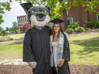 Woman posing with a mascot in a cap and gown