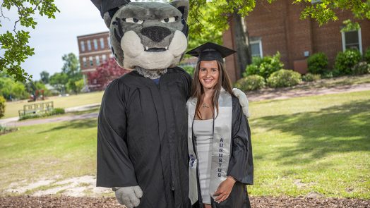 Woman posing with a mascot in a cap and gown