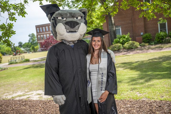 Woman posing with a mascot in a cap and gown
