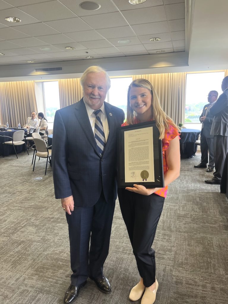 A female college student stands with an older man celebrating an award at a luncheon.