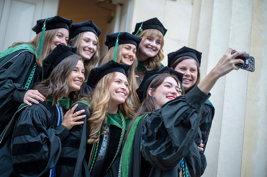 A group of recent medical school graduates pose for a selfie on the steps of an historic building.