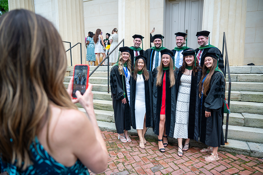 Recent medical school graduates pose for a small group photo as a friend uses a cell phone to take their photo.