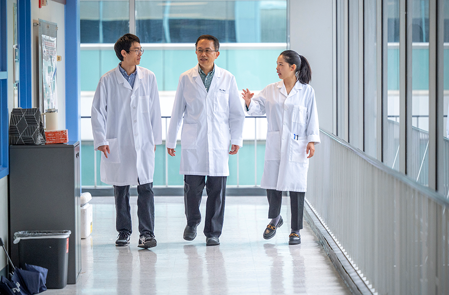Two men and a woman, all wearing lab coats, walk down a hallway in a research building.