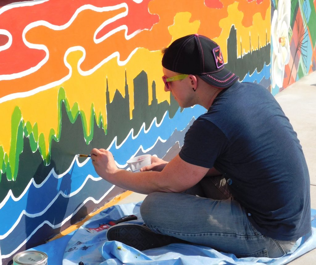 A man paints waves in front of a cityscape as part of a mural.
