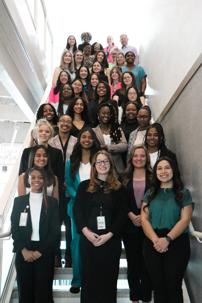 Group of college women stand in a stairway with professional mentors.