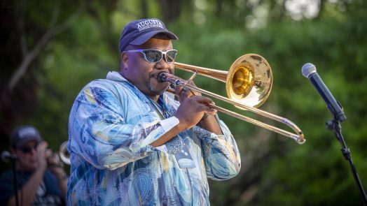 Man plays trombone into microphone at outdoor concert.