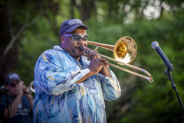 Man plays trombone into microphone at outdoor concert.
