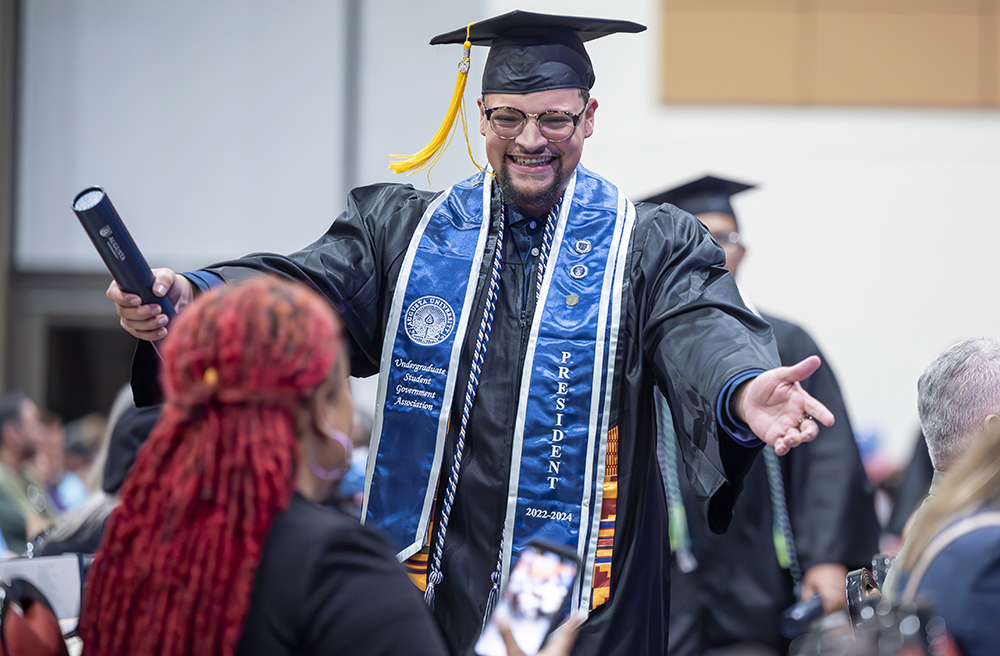 A male college graduate holds out his arms for a hug after receiving his diploma.