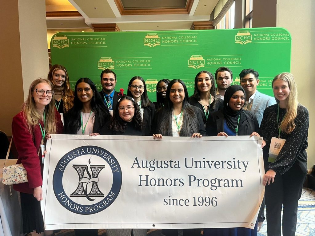 Thirteen college students from Augusta University's Honors Program pose for a photo while holding a banner that reads "Augusta University Honors Program since 1996."