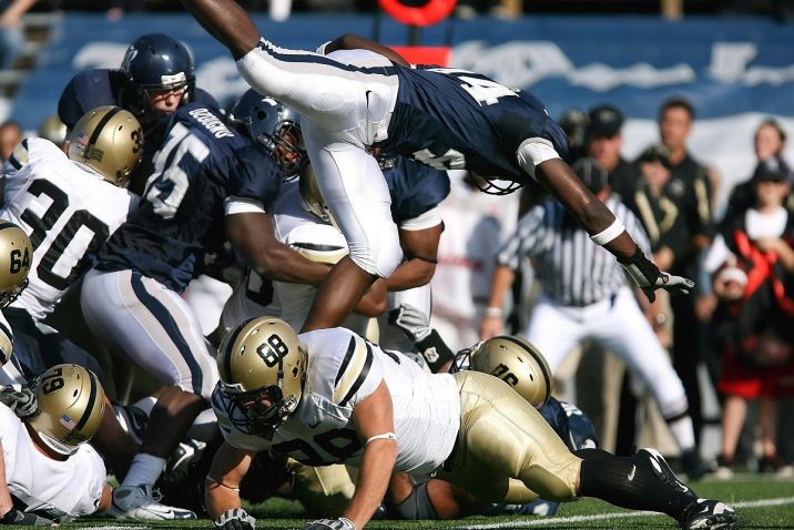 A football player leaps over a pile of players