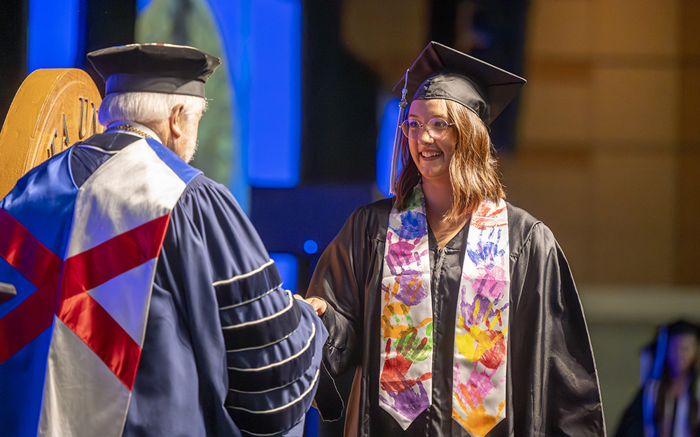 A man in graduation cap and gown shakes hands with a female college graduate.