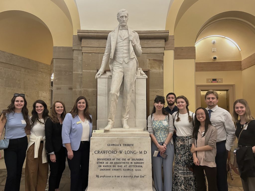 Seven college students and three professors pose for a photo next to a tall statue of Crawford W. Long, MD, in Washington, D.C.