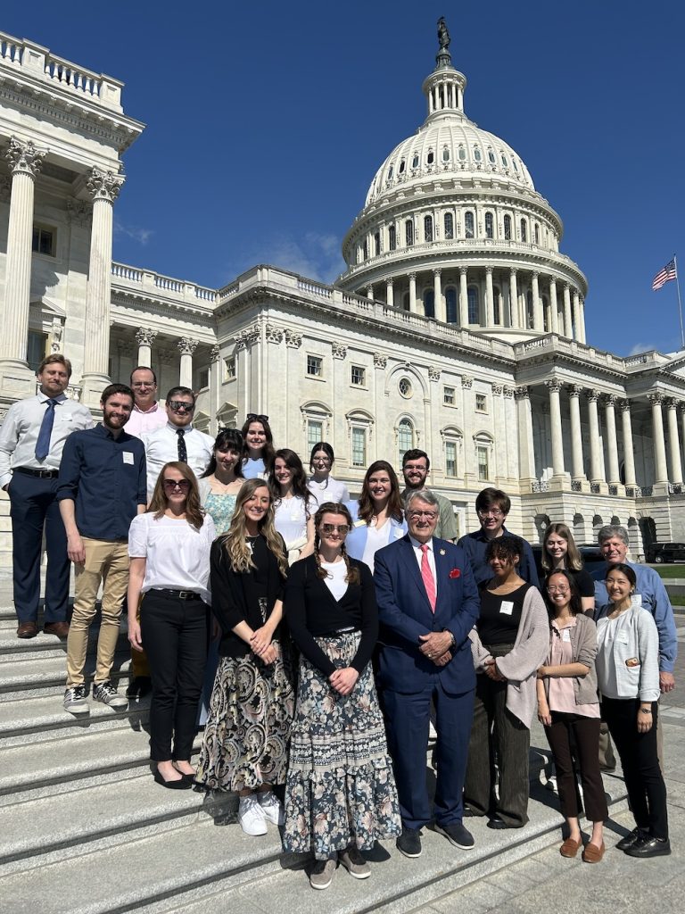 A group of 15 college students and several faculty members pose for a photo with a U.S. representative on the steps outside the U.S. Capitol Building in Washington, D.C.