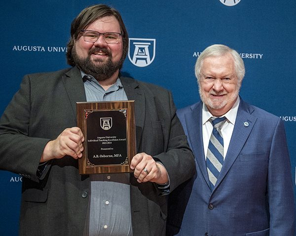 Two men stand together as one holds up an award.