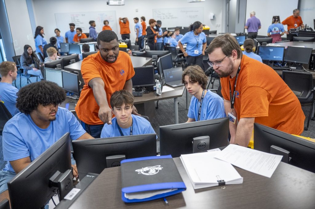 Two camp counselors look over the work of young three men on a computer