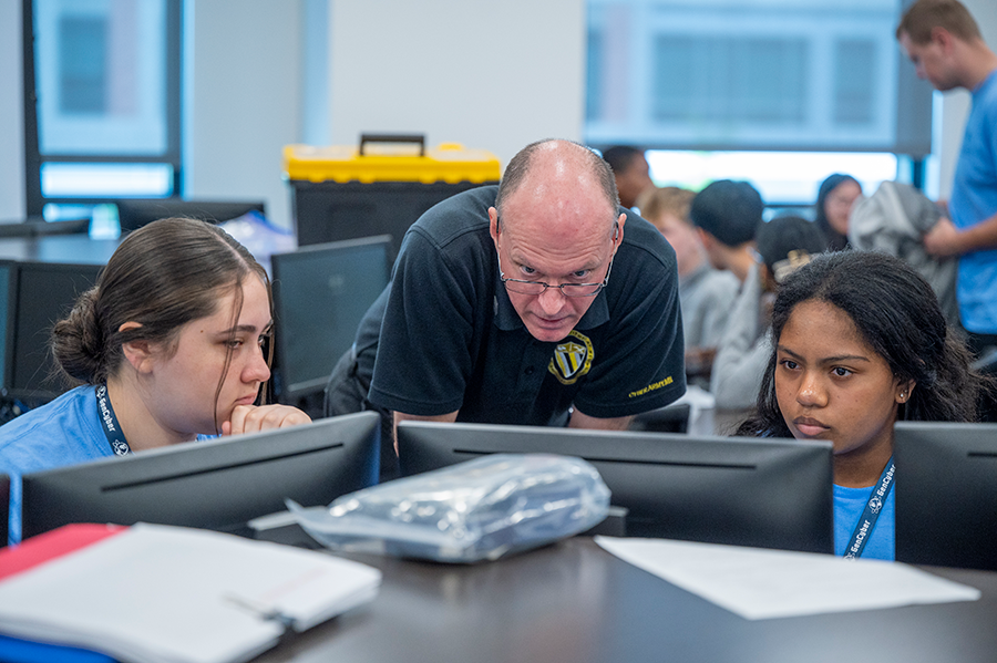 A college professor talks with two female high school students and helps them with a computer program.