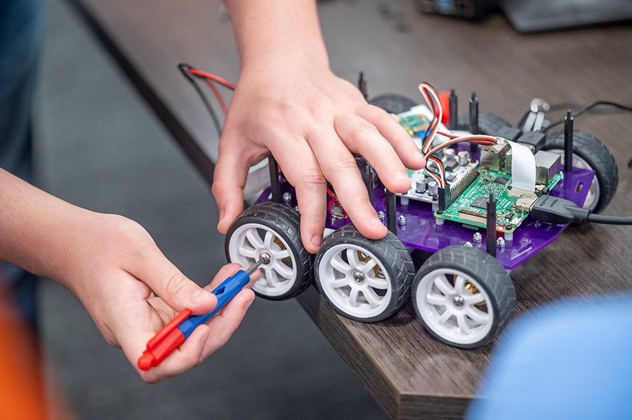 A high school student uses a Phillip's head screw driver to tighten a wheel on a remote-controlled car.