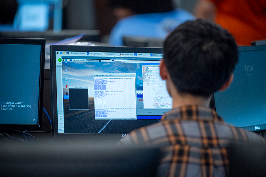 A male high school student sits at a computer and writes computer code in a program on his screen.