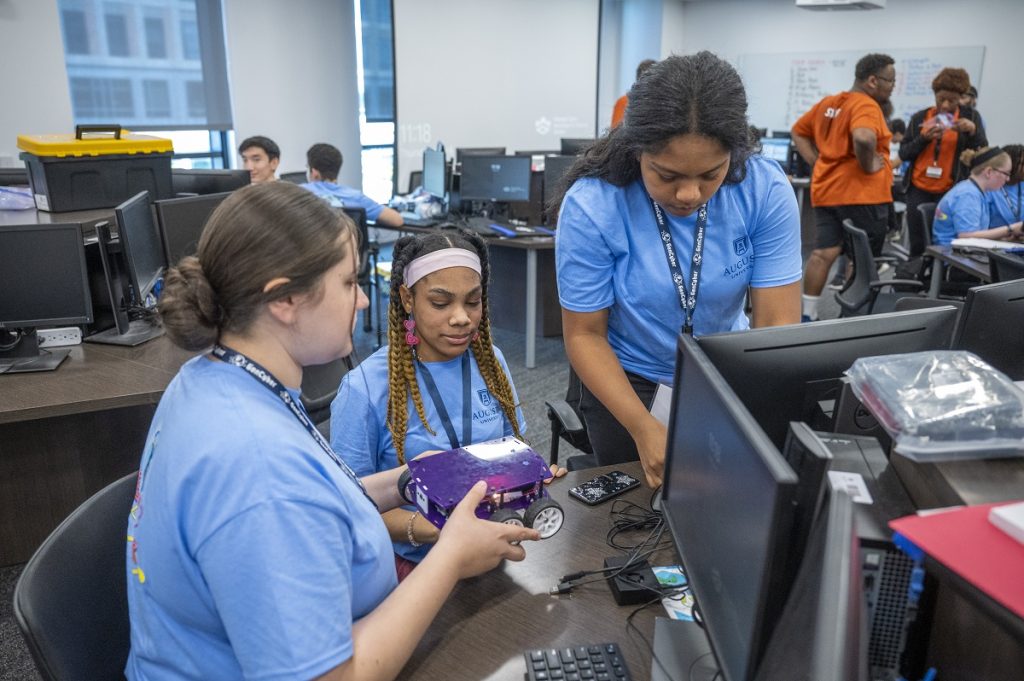 Three high school girls work on programming a robot with wheels